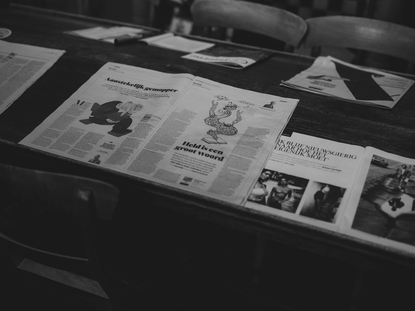 Several open newspapers spread across a wooden table.