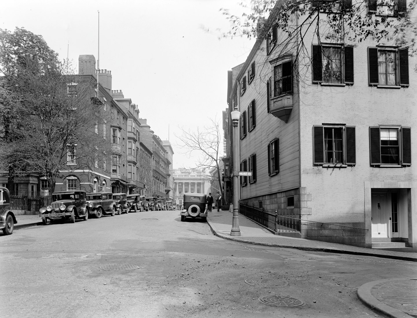 Early 20th-century cars parked on a narrow historic city street.